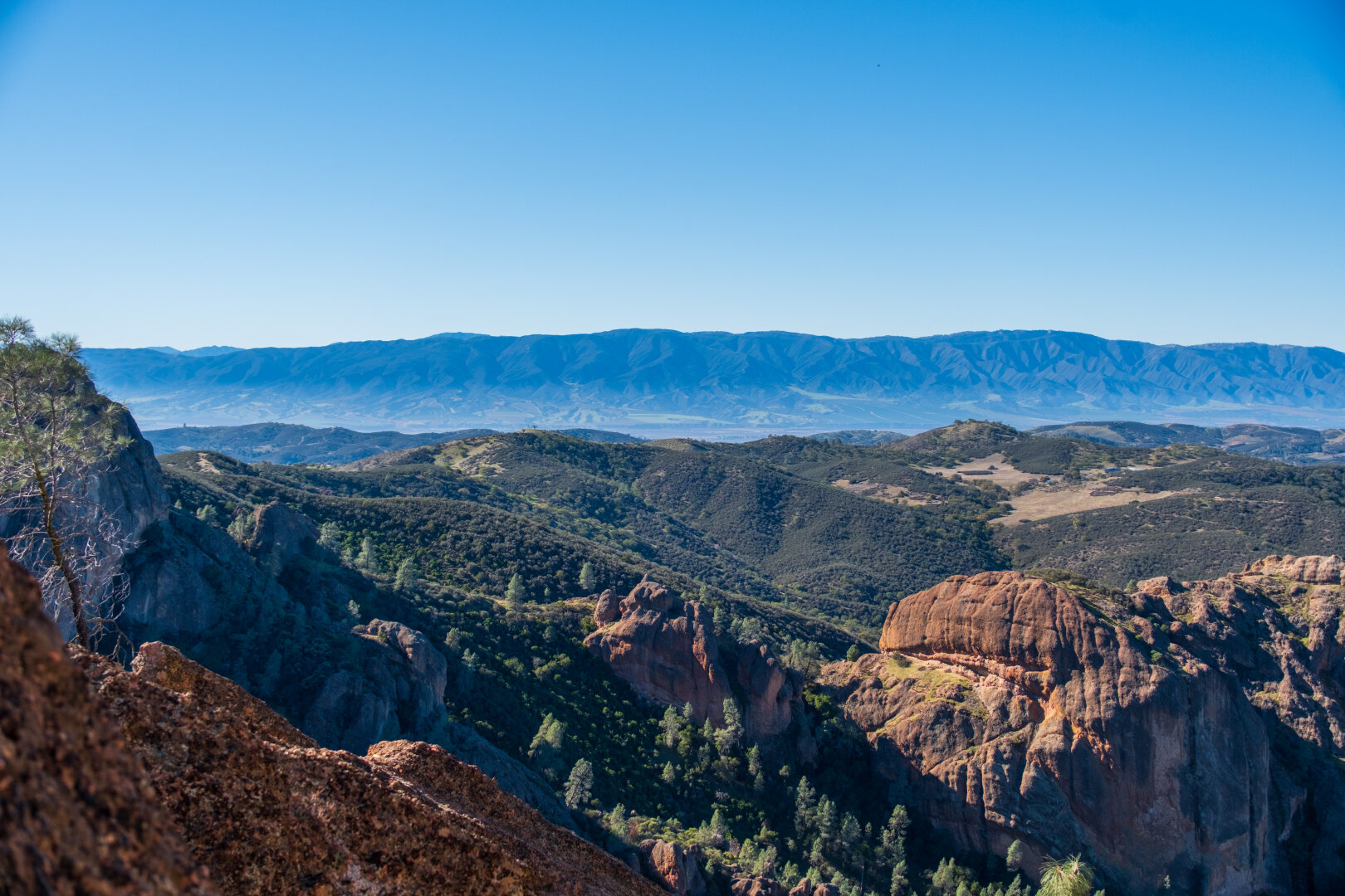 Behind rocky outcroppings, a valley and distant mountains. [Fuji X-T5 / Tamron 18-300]