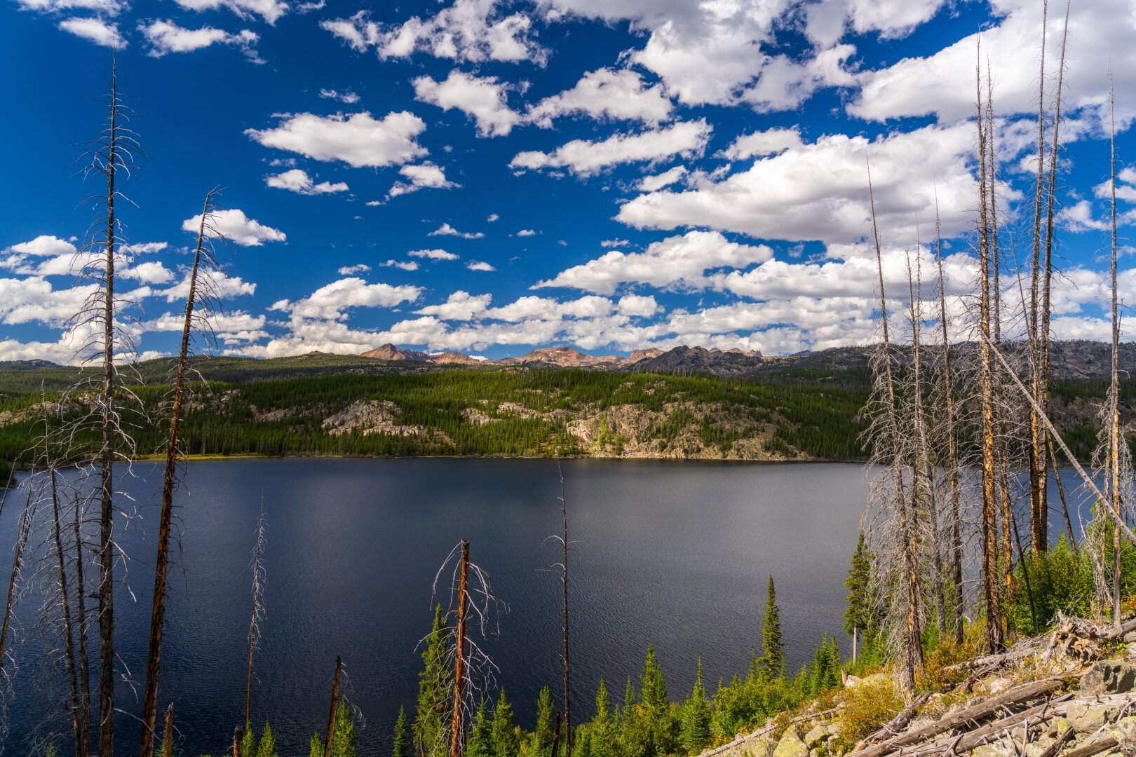 A wide view of a lake with mountains behind and dramatic clouds overhead. [Sony A7R V / Tamron 25-200]