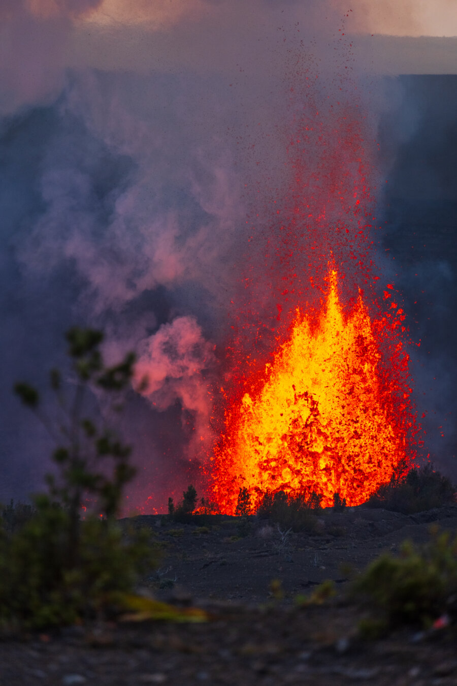 Behind out-of-focus shrubs, a volcano throws lava into the air. [Fuji X-T5 / Tamron 18-300]