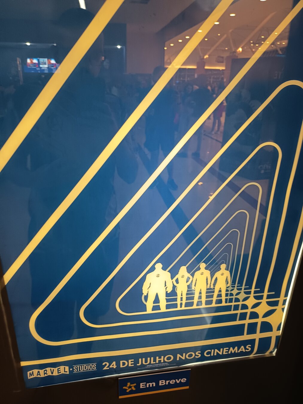 Man takes a picture of a poster from the movie fantastic four first steps, in the picture the man who take the photo is reflected in the poster posing with four fingers making an reference to the fantatic four