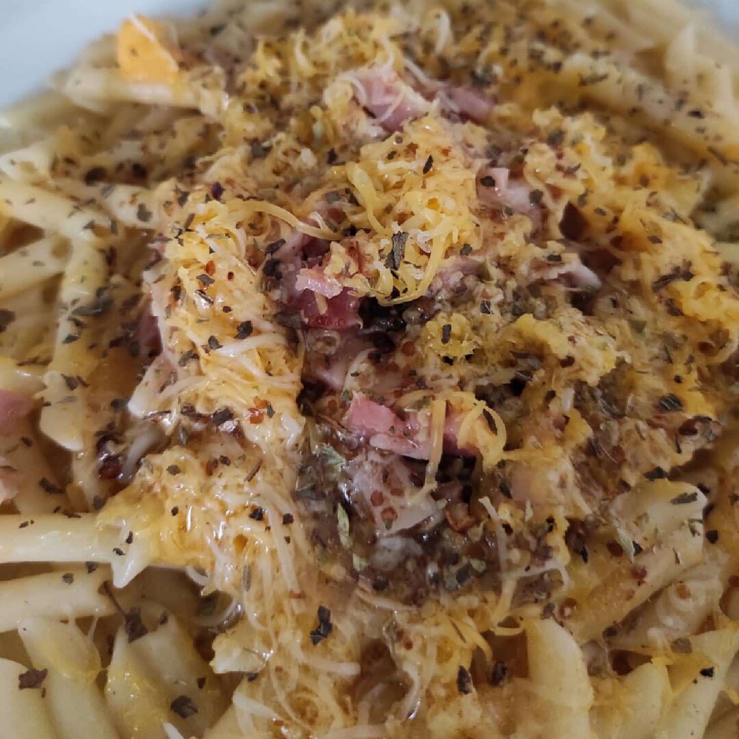 Detalle del Centro del plato desde arriba. Se aprecian las texturas del queso fundido y los contrastes de color con el orégano y albahaca y otras especias, pasta y queso y el bacon.