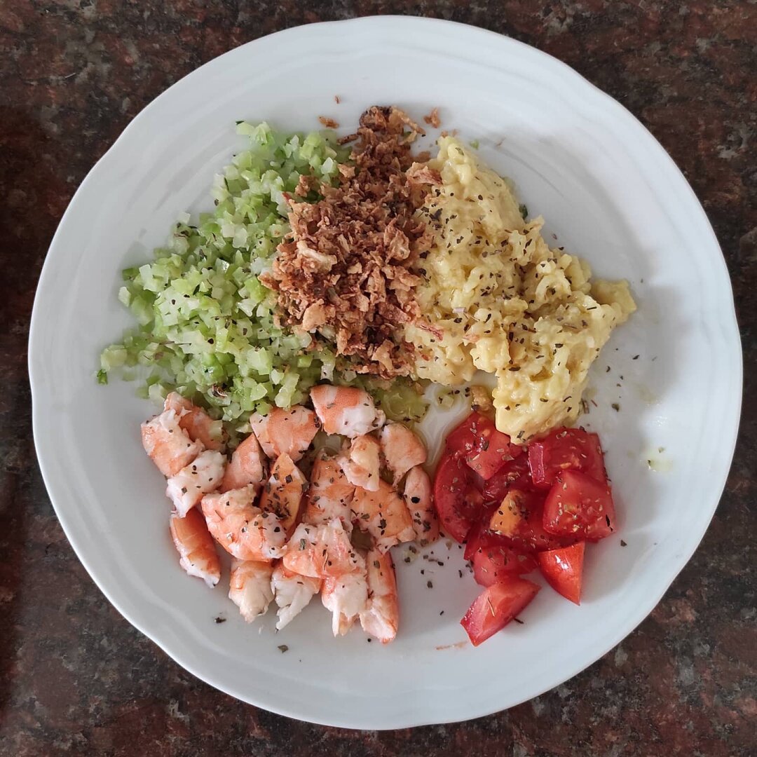 Emplatado de la comida abajo tomate a la derecha y langostinos cocidos y troceados a la izquierda, arriba brócoli en daditos, y en medio crujiente de cebolla y a la derecha el arroz.
