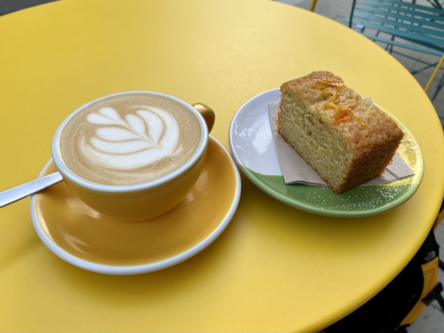 Cup of cappucino showing flower in milk, with puece of cake, on yellow table