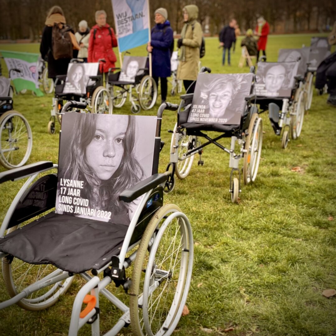 Five (out of hundred) wheelchairs in a row, each with a BW photo of a longcovid or other PAIS patient who could not attend, on the Malieveld in The Hague, The Netherlands