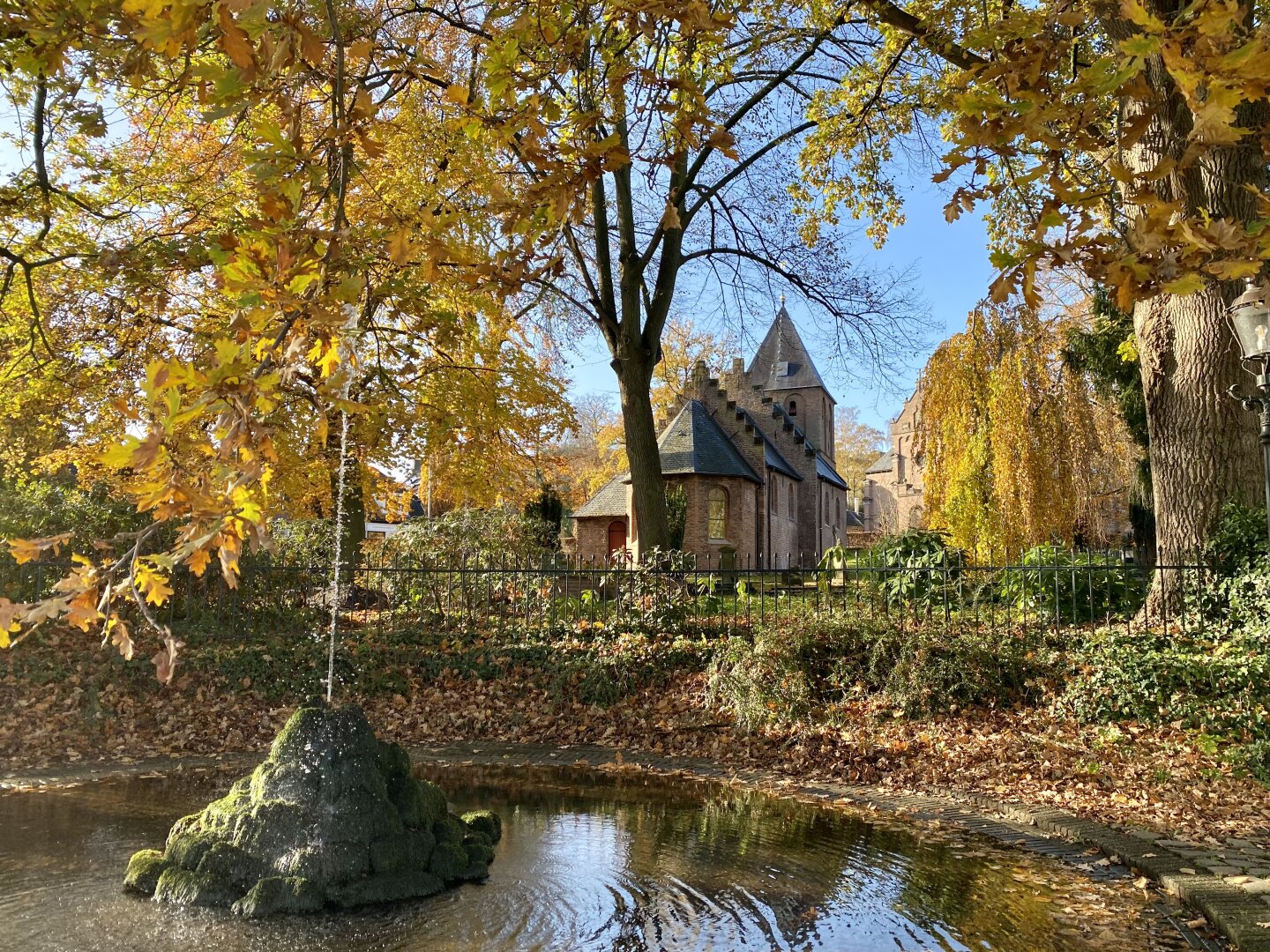 Pond with fountain, with chapel at the back, all in bright sunny autumn colors
