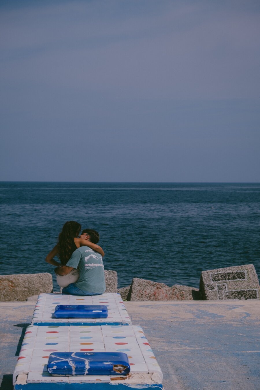 a young couple kissing while sitting on a stone close to the sea