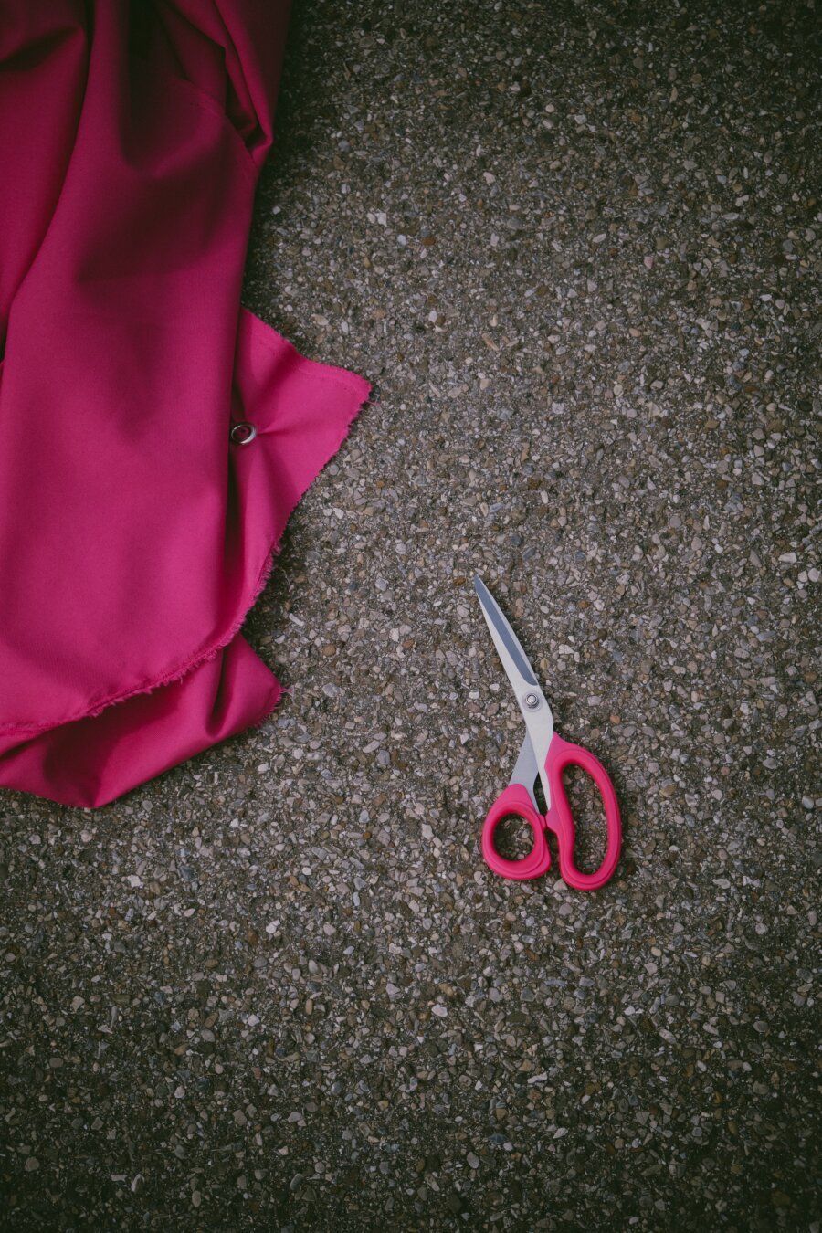 pink scissors lying next to a pretty big piece of cloth (pink, too) on a concrete floor. someone seems to be working with both and at the moment is taking a break.