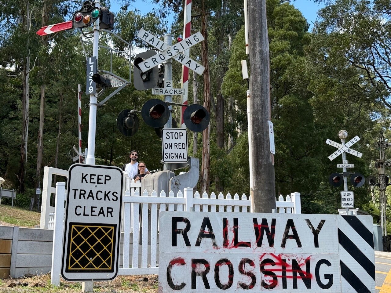 A view of all of the extensive railway crossing signage just outside of Belgrave Station. Older signs with vintage fonts saying “RAILWAY CROSSING” sit next to modern signage that indicates you should not stop on the hatched yellow boxes. There are also older train signals with lenses and tails, next to more modern LED crossing warning lights.