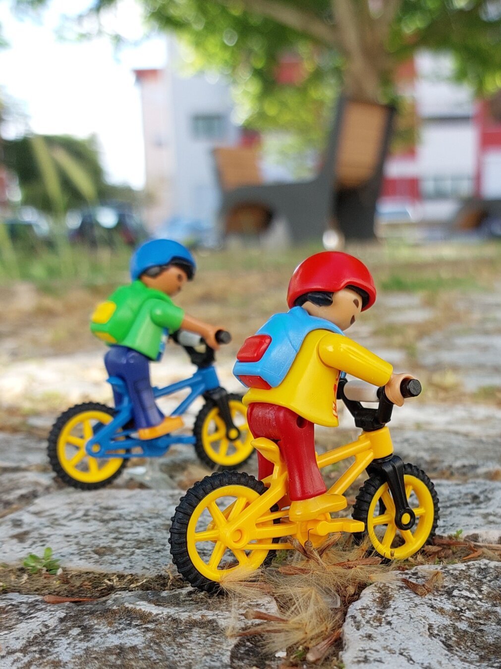 Duas crianças playmobil em bicicleta com mochilas nas costas.