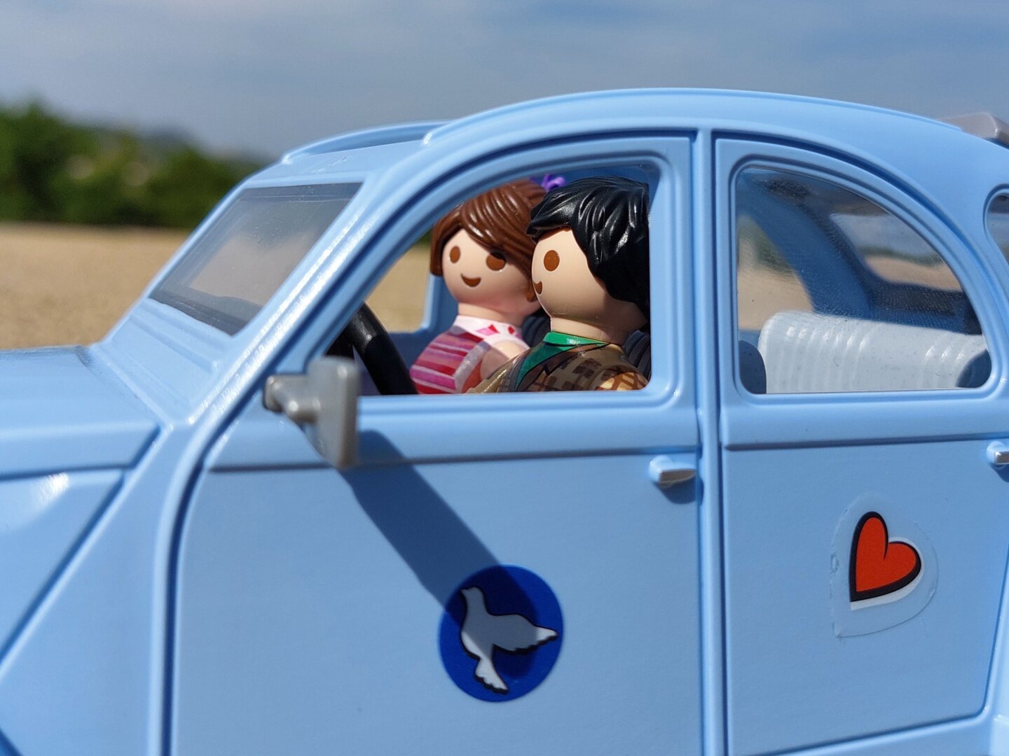 Um casal playmobil apaixonado dentro de um citroen 2cv antigo, azul.