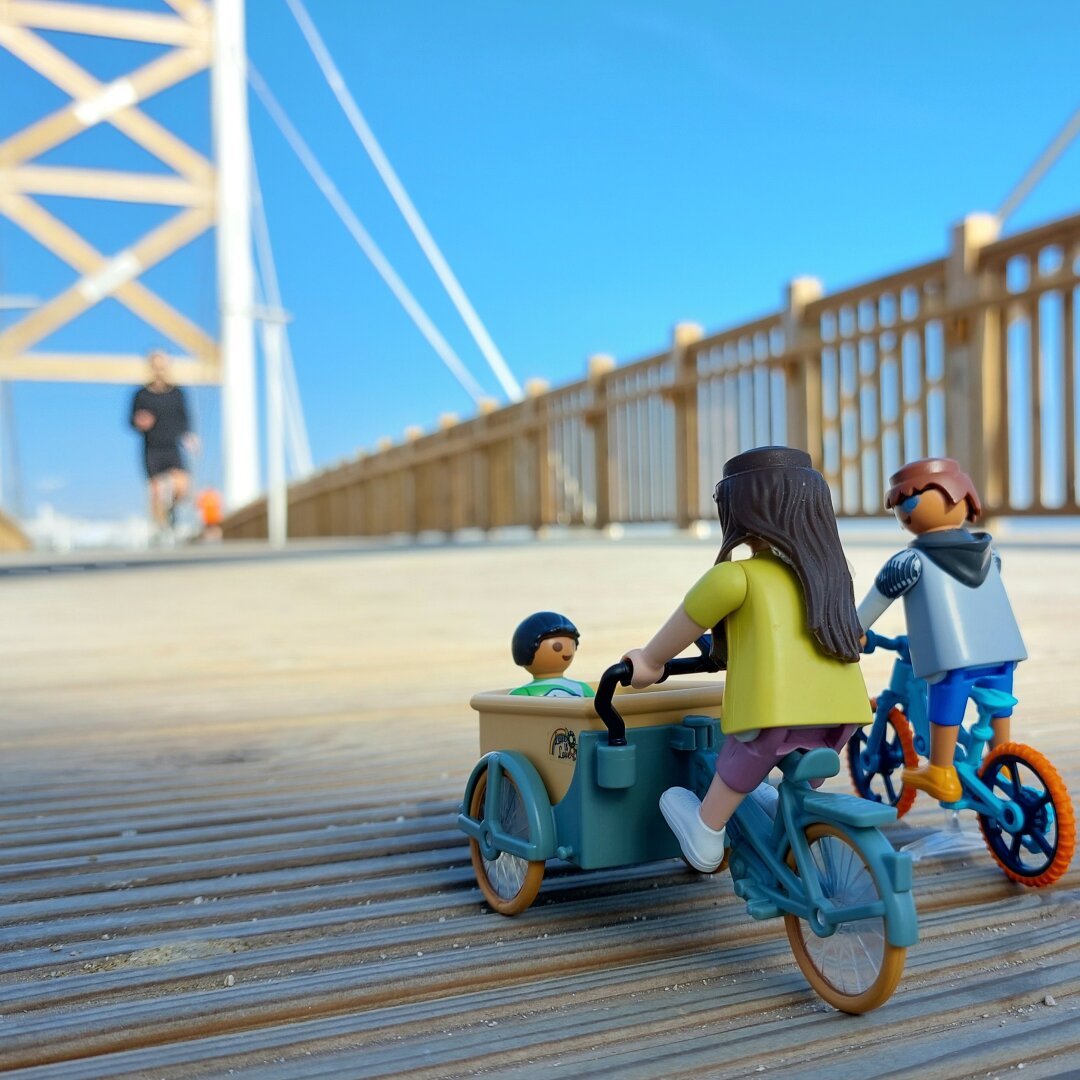 Família playmobil em bicicleta de carga numa ponte de madeira e um homem a correr