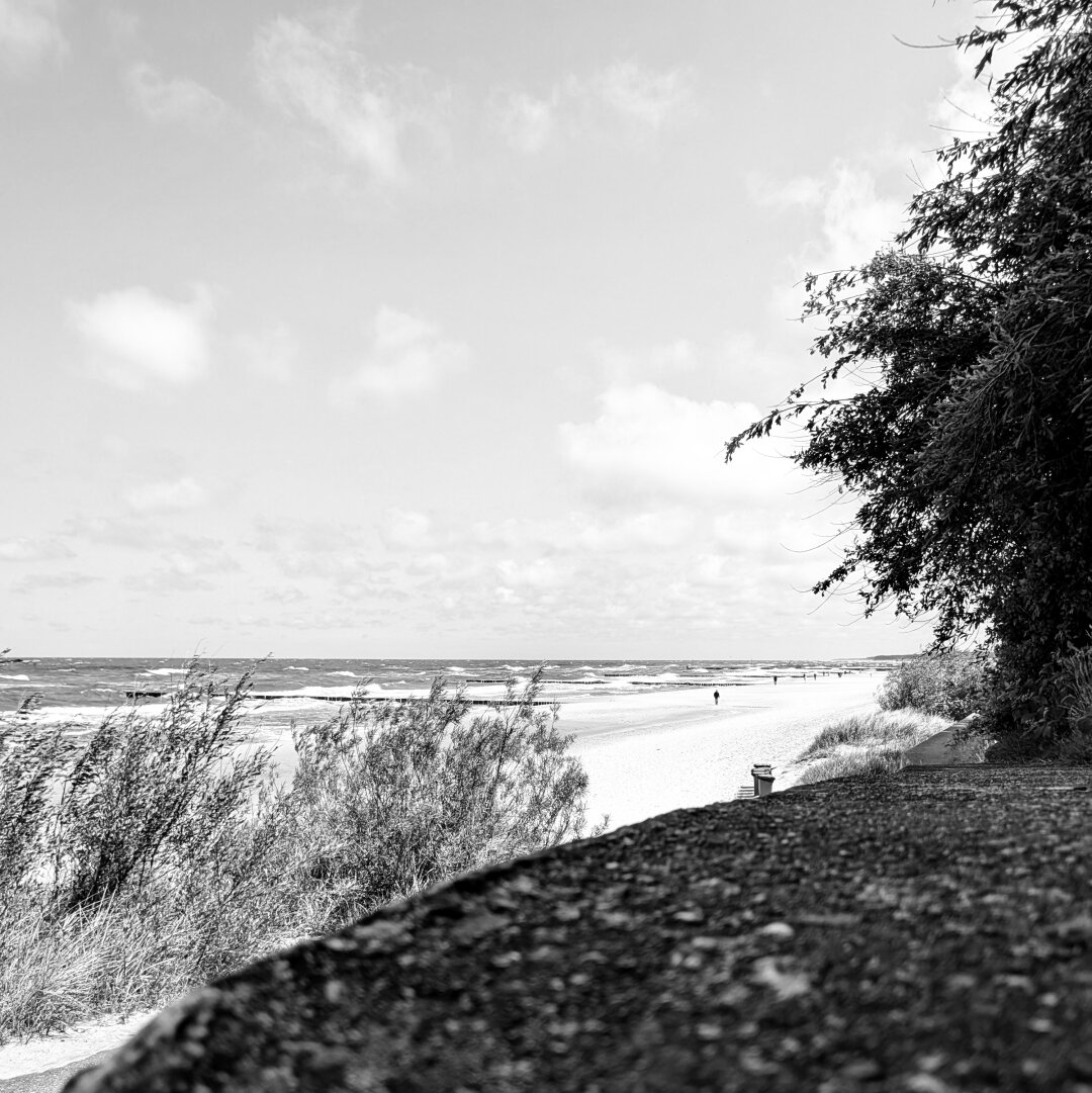 black and white photo of the sea shore beach the view goes over a little wall in the foreground and the beach and stormy wavy sea in the background
the focus is on the background