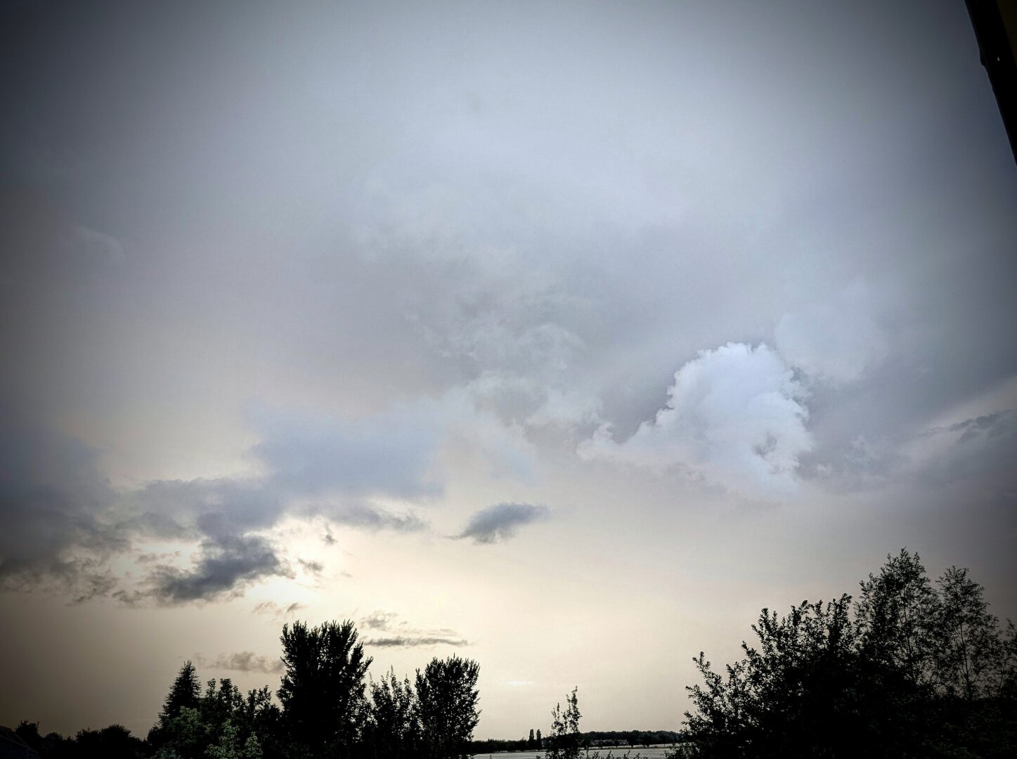 near black and white photo of a cloudy sky, that has a really strange glow to it. the clouds are part of a storm front rising up while the sun sets.
