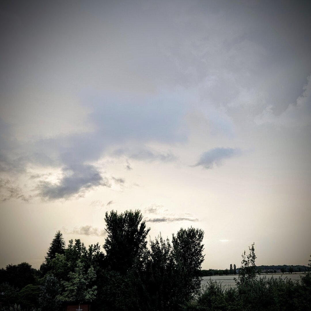 near black and white photo of a cloudy sky, that has a really strange glow to it. the clouds are part of a storm front rising up while the sun sets.