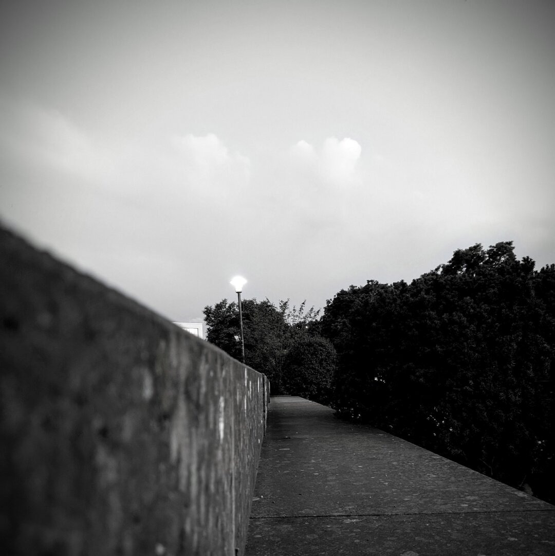 black and white photo of a park and the sky on a evening shortly after sunset. the view following the edge of a stairstep torwards a streetlight.