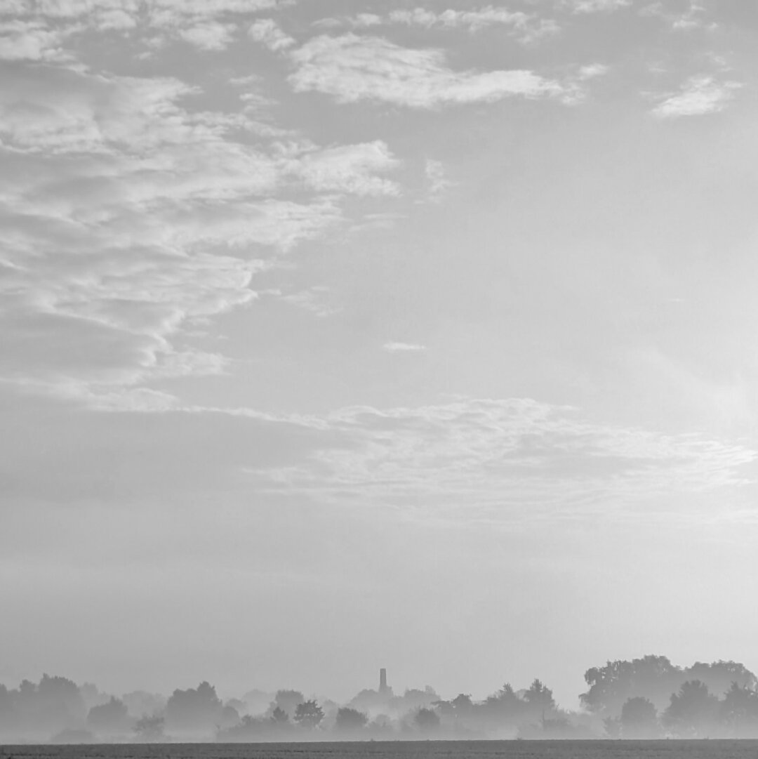 black and white photo of an foggy landscape. the scene is dominated by the slightly cloudy sky wich takes 2/3 of the image.