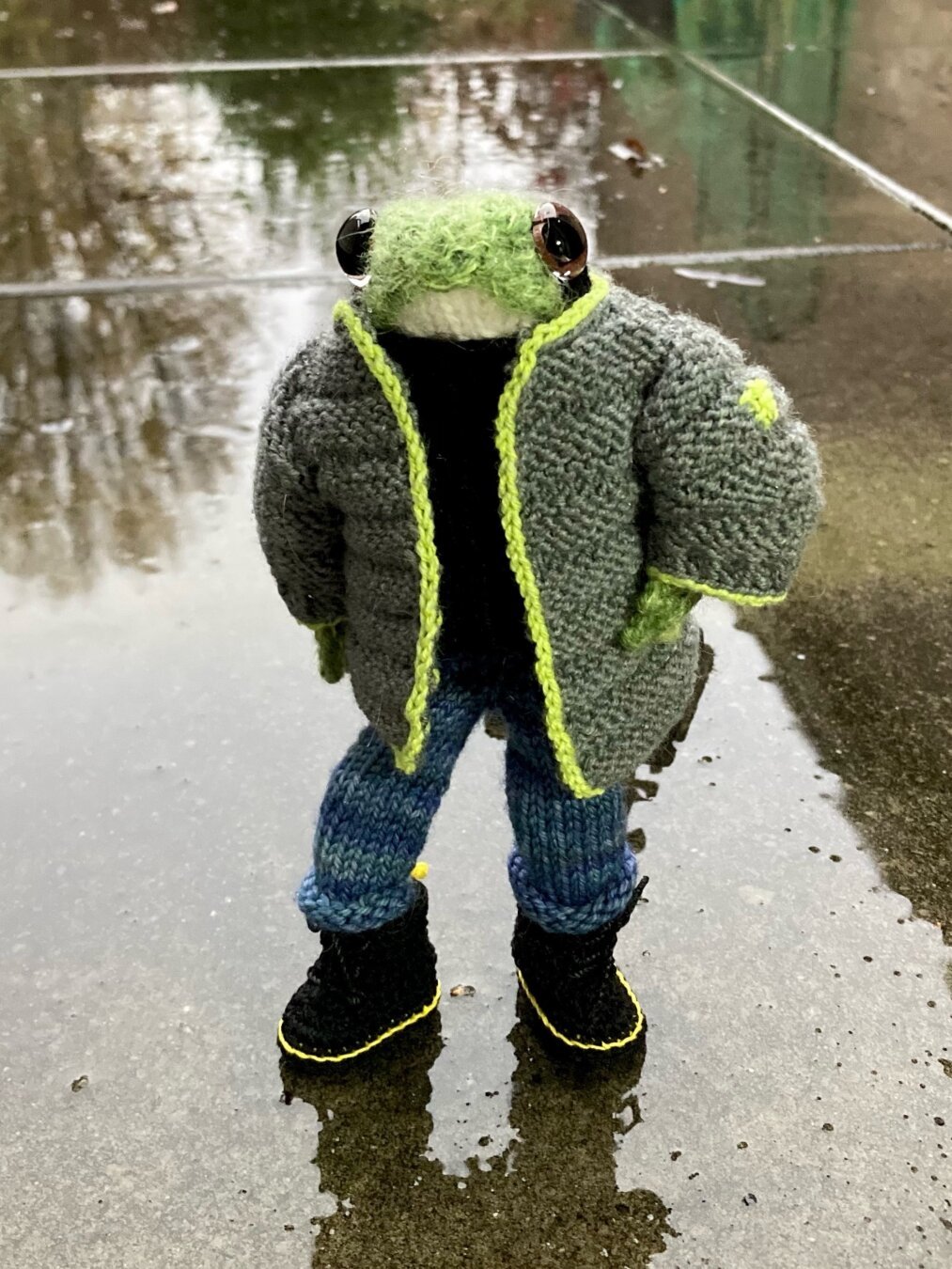 knitted frog wearing knitted gray puffer jacket with yellow accents