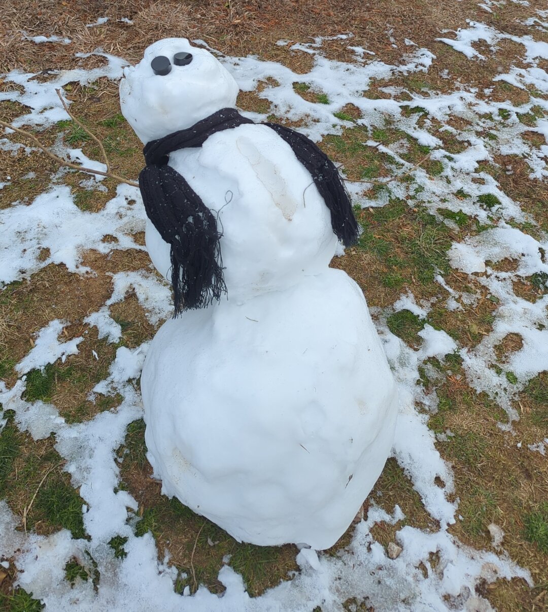 A partly melted snowman leaning back