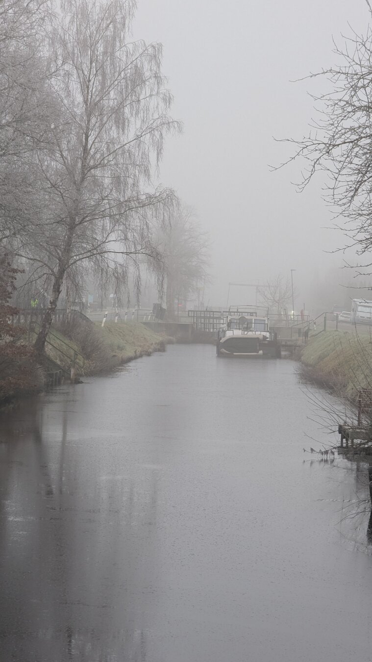 Der Fehnkanal von Wilhelmsfehn im Nebel. Direkt vor der Schleuse liegt ein Schiff mit dem Namen Hoffnung.