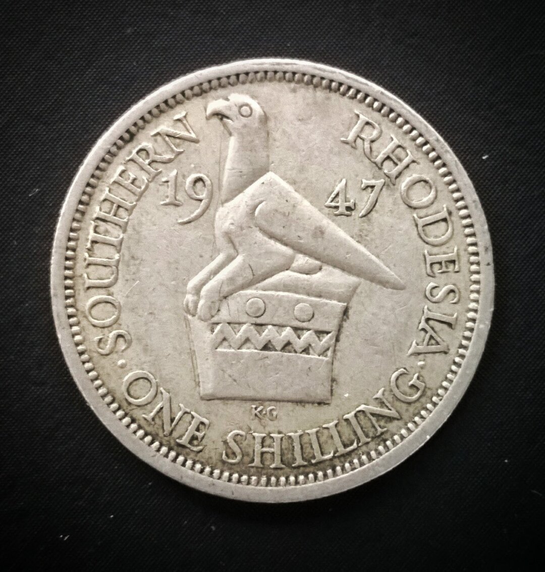 Moneda de 1 Chelín.
Rhodesia del sur (colonia británica, 1947).
Motivo del reverso: Ave "Gran Zimbabwe".