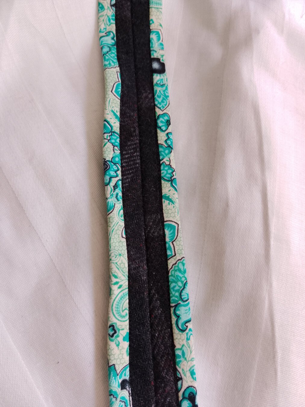 Photo eines Ärmels von innen. Der Stoff rechts und links ist weiß, die Nahtzugabe ist in dunkelblauer Wolle, die Kanten der Nahtzugabe ist mit einem grün gemustertem Stoff umfasst.