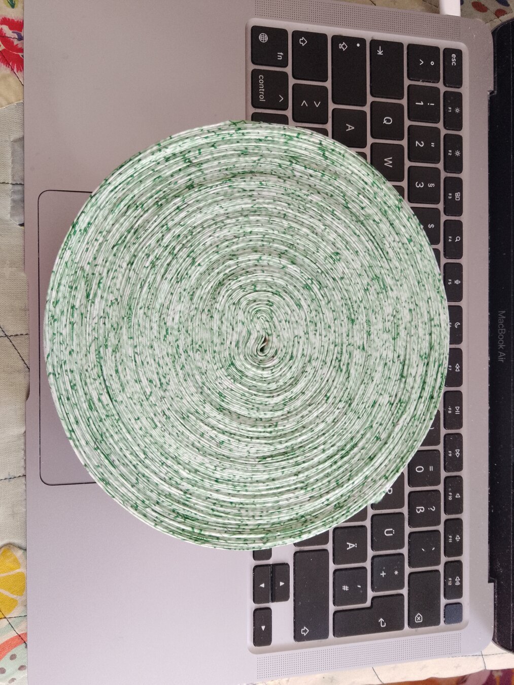 A large, 17cm diameter, circle of rolled up bias tape. the bias tape is made out of green/white fabric with little flowers. The whole disc is on to of a laptop keyboard.
