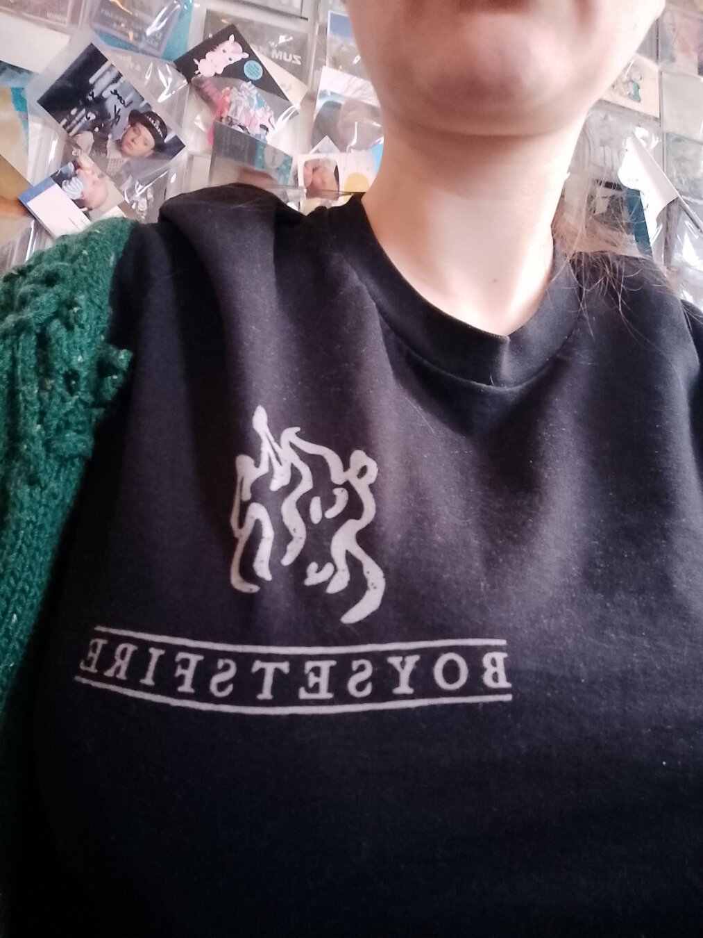 Frauenoberkörper mir einen schwarzen T-Shirt. Shirt hat den Aufdruck einer kleinen Flamme mit boysetsfire drunter.