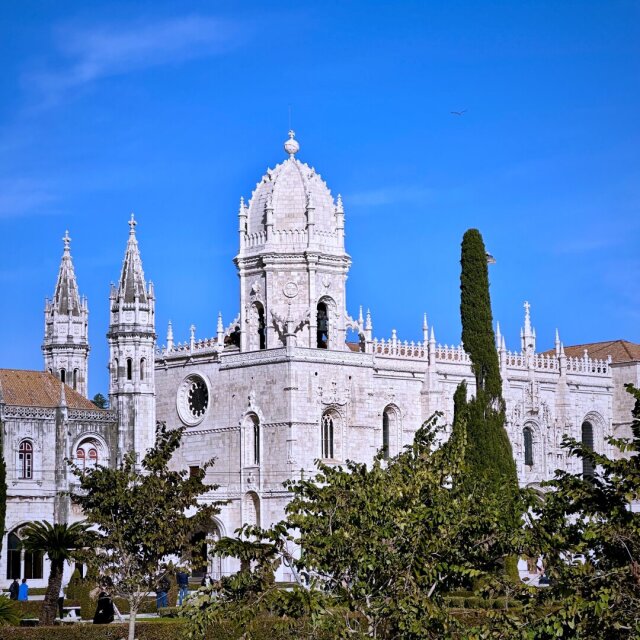 El monasterio de los Jerónimos visto desde el jardín: piedra blanca calada, torres con agujas labradas como encajes, rosetón ciego, una cúpula bulbosa al centro. Delante, un ciprés altísimo perfectamente vertical, como aguja que cose el edificio al cielo. Cuesta creer que algo de piedra haya tardado tantos siglos en aprender a no parecer pesado.