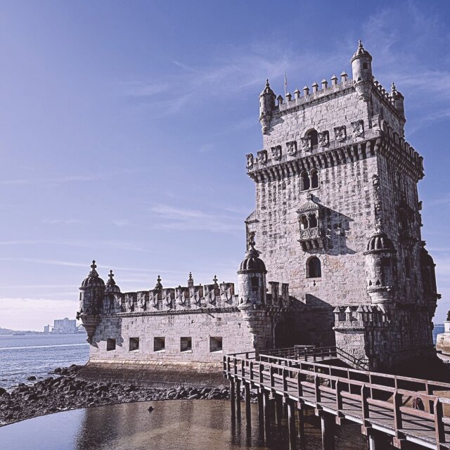 La Torre de Belém al sol de invierno: piedra blanca de fortaleza manuelina, almenas, garitas en cada esquina y un trozo de bastión avanzado sobre el río. Una pasarela de madera la conecta con la orilla, llana y reciente. Antes vigilaba a quien salía; ahora vigila a quien se queda. La función cambia, la silueta no.
