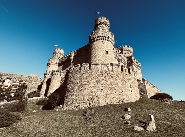 Castillo de granito visto desde abajo, torre del homenaje rematada con bolas isabelinas, almenas matemáticas y muros que beben la luz seca de enero. La bandera apenas se mueve en lo alto. Una fortaleza que ya no defiende nada y por eso se deja mirar.