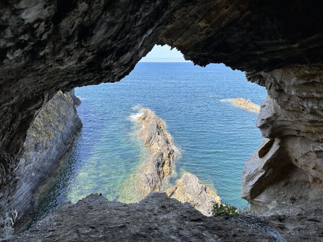 Boca de cueva a contraluz que enmarca el océano: aguas turquesa transparentes, una arista de roca emergiendo, horizonte limpio. La piedra hace de visor, recorta el mundo a la medida del marco. Quien ha vivido bajo techo entiende que la ventana es una forma de dosificar la inmensidad.