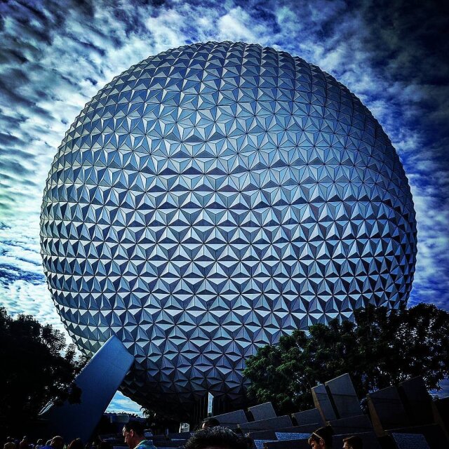 Spaceship Earth: una esfera geodésica gigantesca cubierta entera de triángulos plateados, recortada contra un cielo de nubes nervudas. En la base, hojarasca tropical y unas cabezas mínimas haciendo cola. La utopía geodésica de 1982 sigue brillando, aunque la cita prometida con el futuro ya quedó atrás.