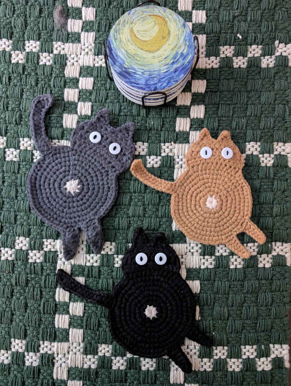 Three crocheted coasters with their buttholes in the center. An orange one, a dark one, and a gray one, one for each of my cats.