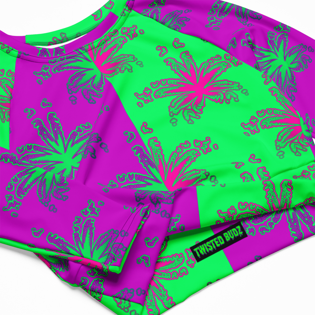 A closeup of a long-sleeve crop top shirt with a weird weed leaf pattern. Half of the design has green cannabis leaves with a purple background in a repeating pattern. The other half has hot pink pot leaves with a mint green background.