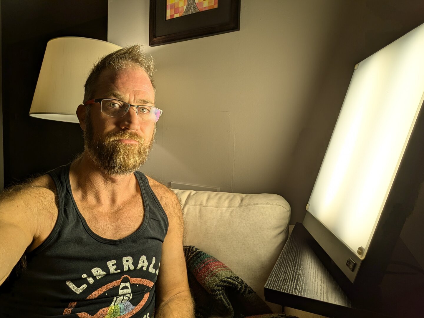 White guy with glasses sits in a chair next to a big ass light box. He is not happy.