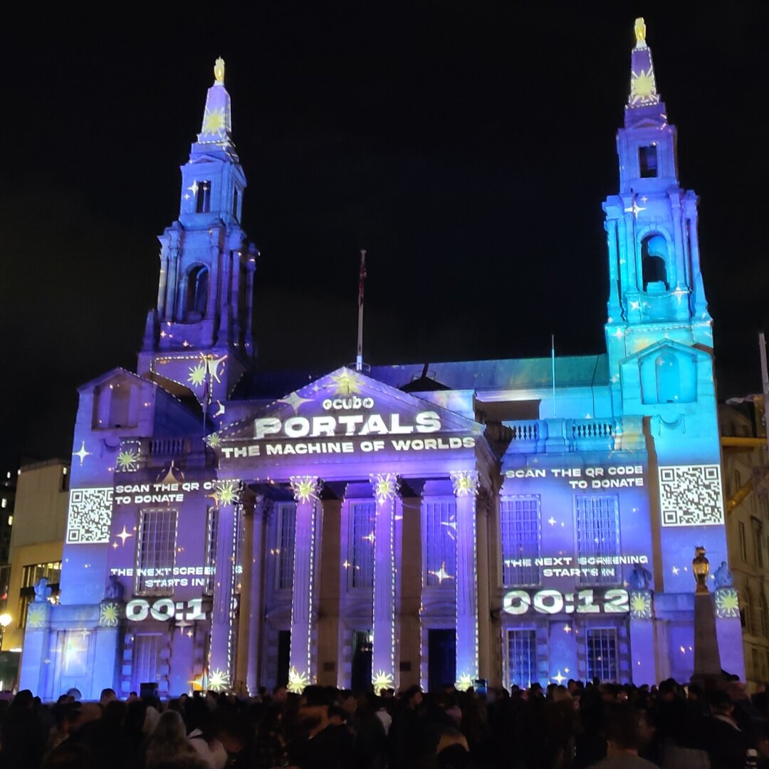 Leeds Civic Hall lit up with a spacey projection mapping advertising the next showing. It is all purple and blues with dashed lines drawn around prominent features like columns and windows.
