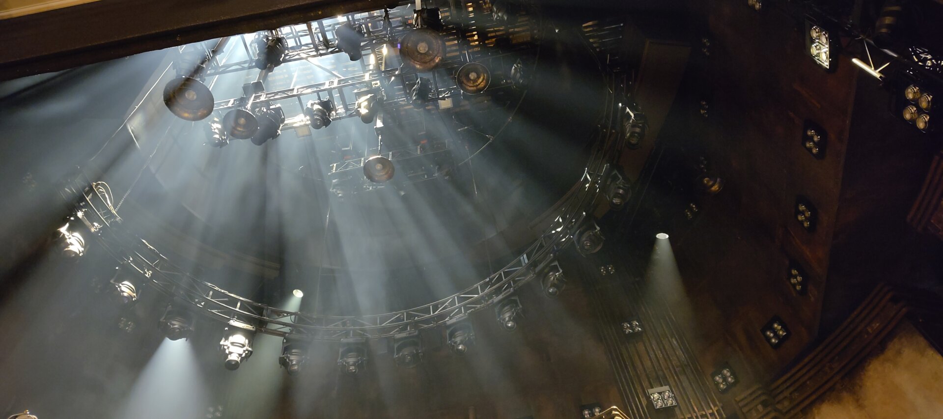 Looking up into the area above a West End stage towards lighting rigs. There's dry ice making dramatic shadows radiating outwards.