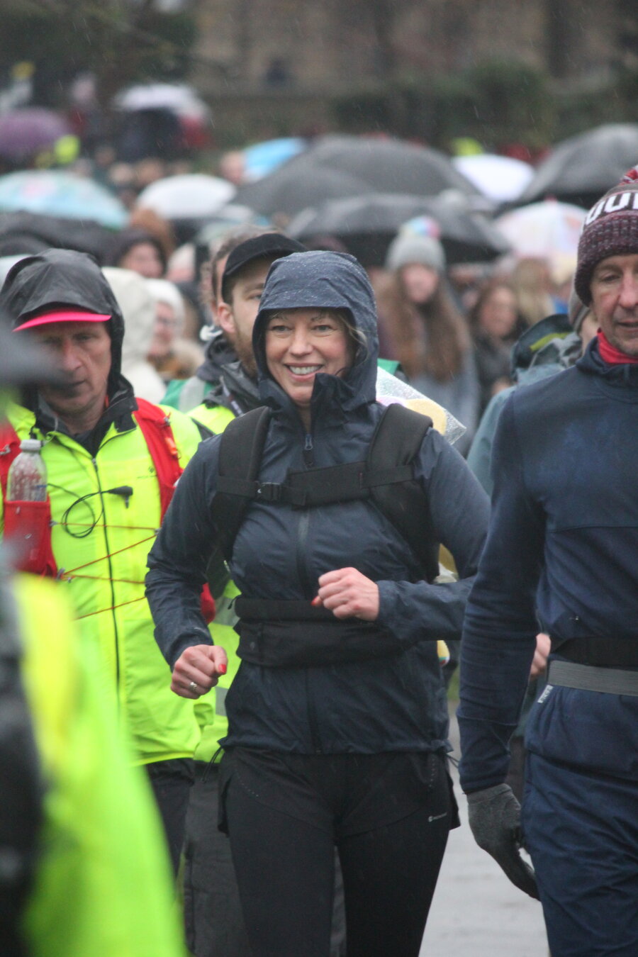 Sara Cox  running in a rain jacket through Horsforth Hall park surrounded by people