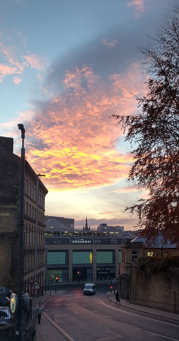 A view towards Bradford Broadway shopping centre. Above are dramatically underlit rippled clouds in hues of gold, pink and purple.