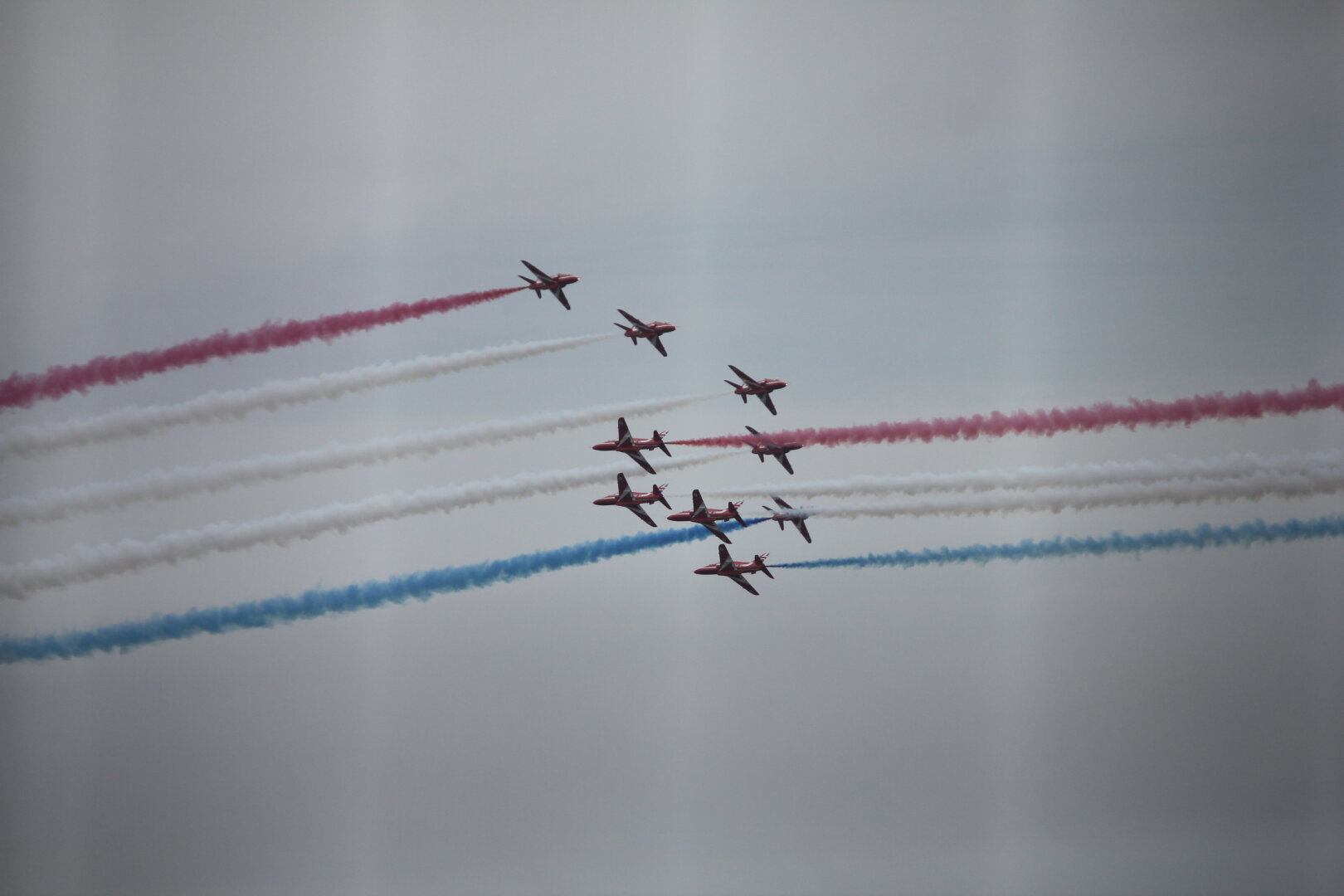 Five Red Arrows flying in a 'v' from the left cross paths with four flying from the right. All have smoke trails.