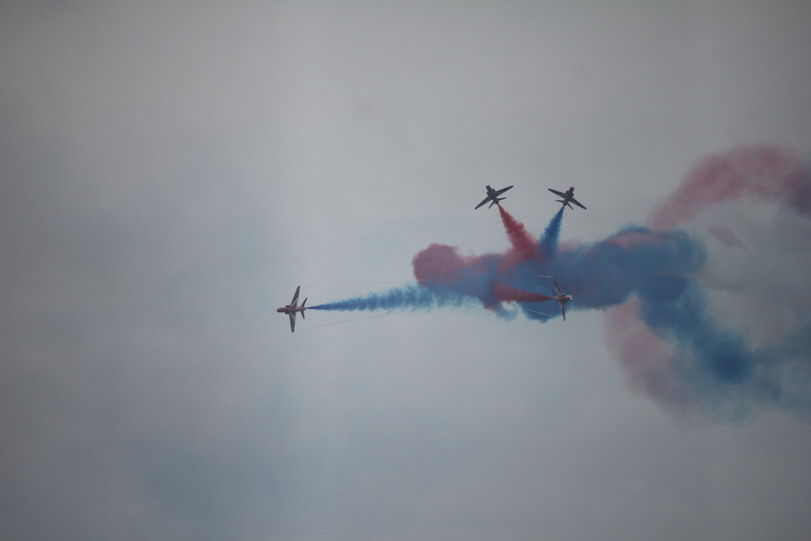 Four Red Arrows burst out froma clump of blue smoke each with a smoke trail behind