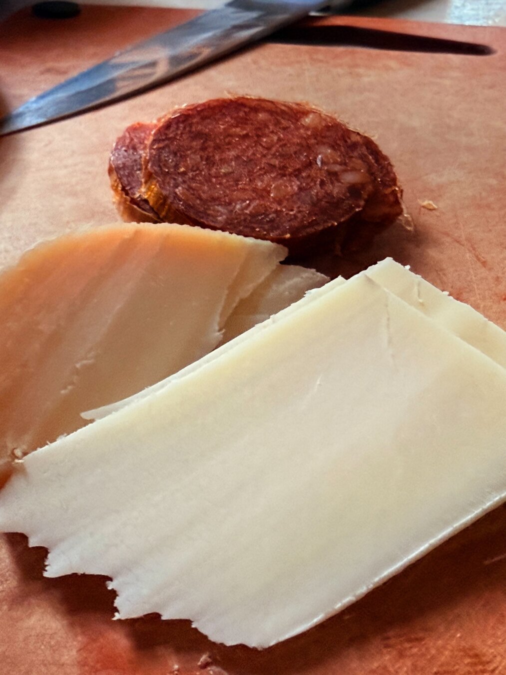 Spices of two kinds of cheese and a spicy sausage on a cutting board with a knife in the background