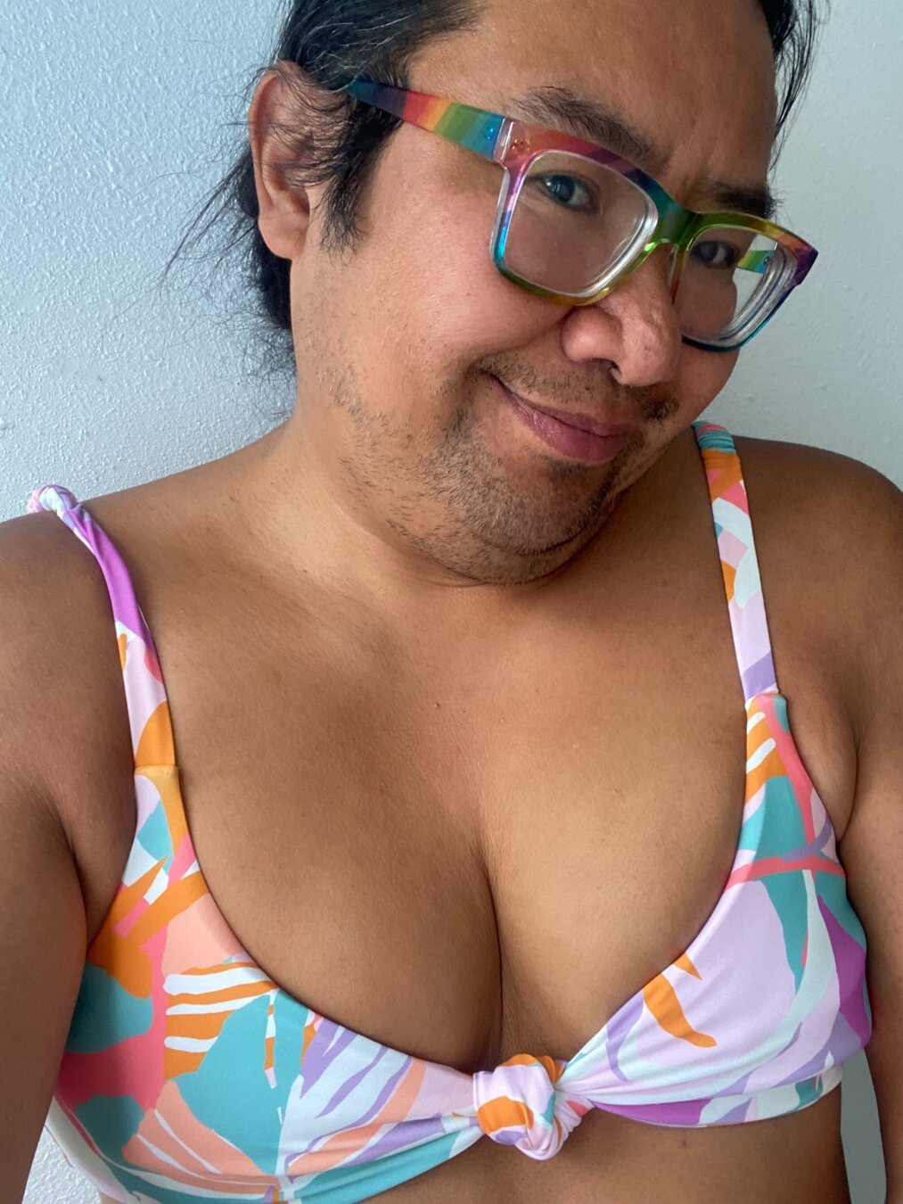 Selfie of a tanned person with rainbow glasses wearing a pastel floral bikini top