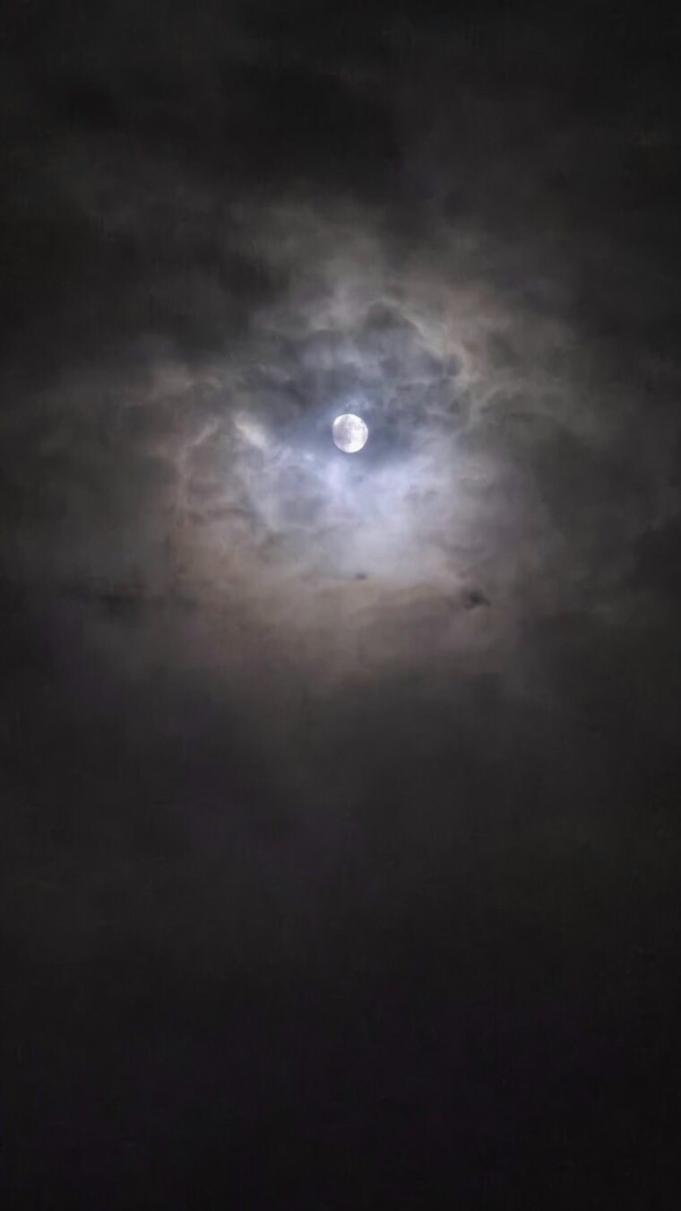 The moon behind some clouds at night. The moon is so bright it's as if it's the sun peaking out.