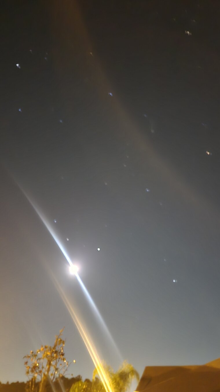 A photo of the moon and the sky, with light refracting a bright orange glow in two places on each side of the picture. Bright white stars are in the dark background.