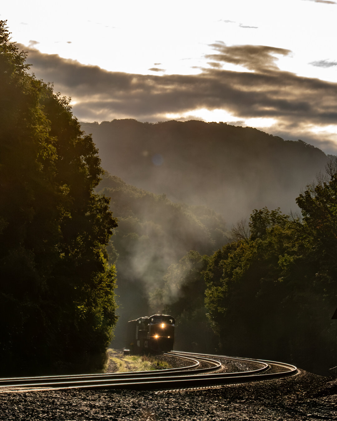 In a foggy mountain area with harsh light and shadow, a train makes it way through