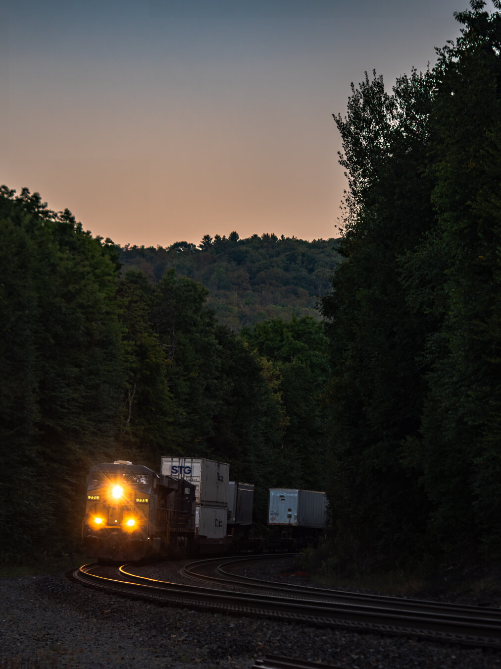 At dawn or dusk, a train with three headlights coming down a rail track