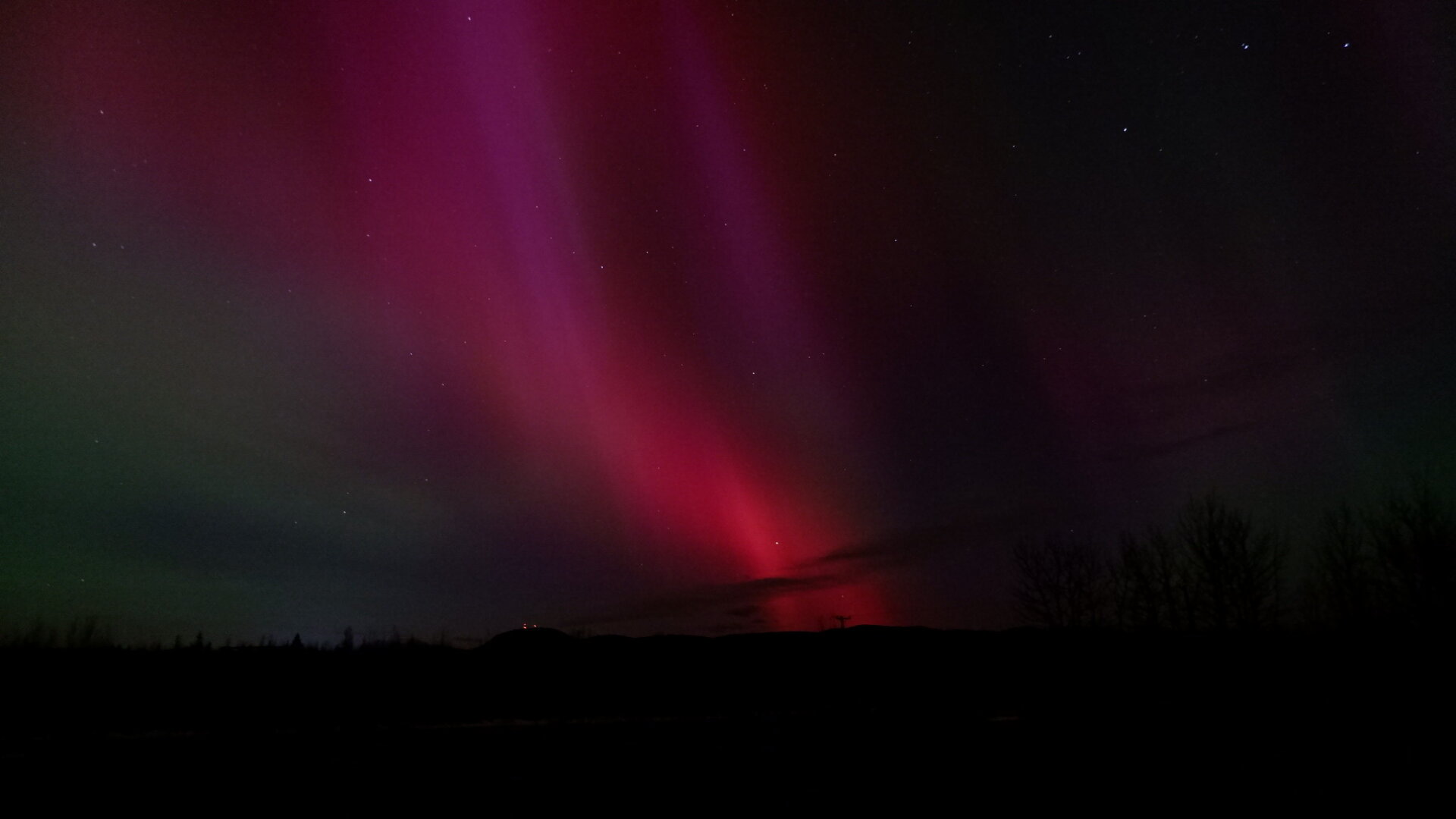 Showing bright aurora in the night sky. Mostly red, pink and green along the edges.