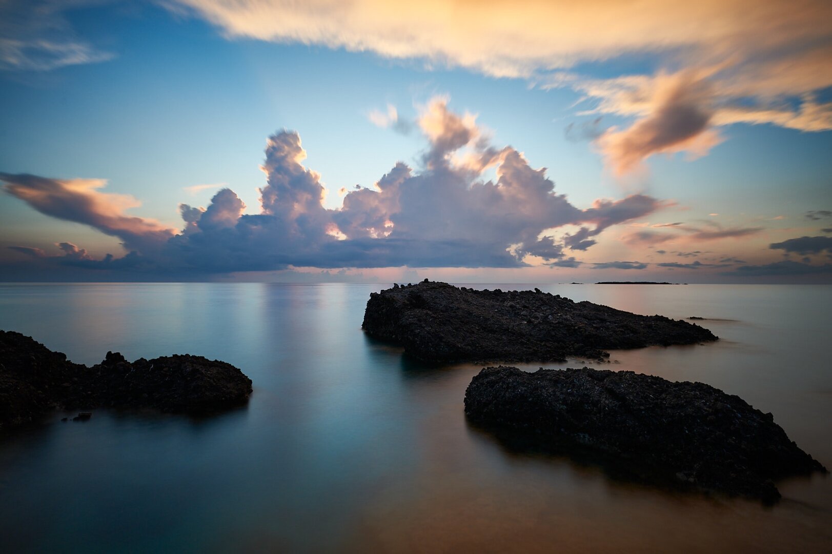 The photo is divided in the middle by the horizon, the upper half shows the sky, the lower half the sea with three rocks.