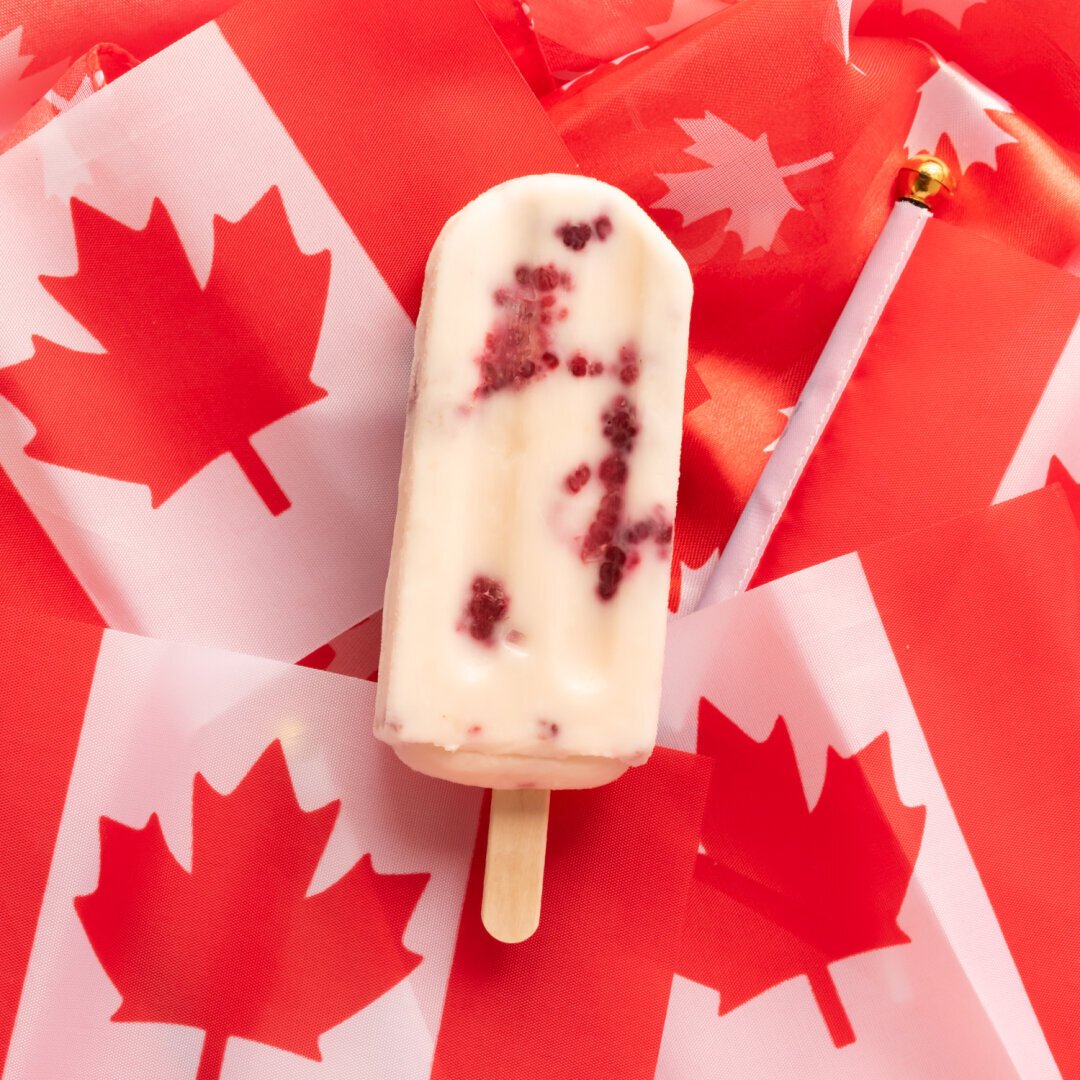 A creamy popsicle with raspberries in it on a background of small Canadian flags